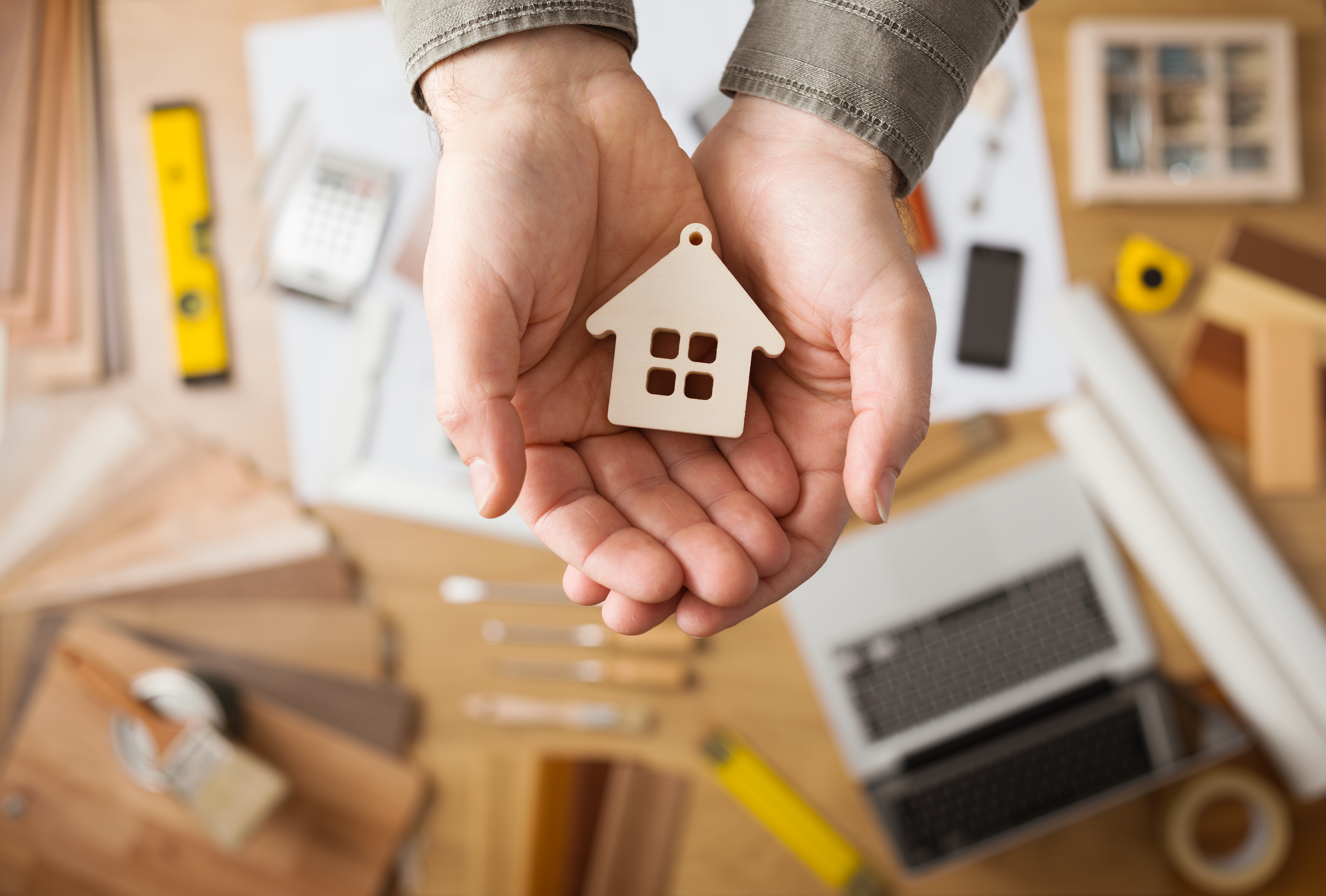 A persons hands holding a small wooden cutout of a house